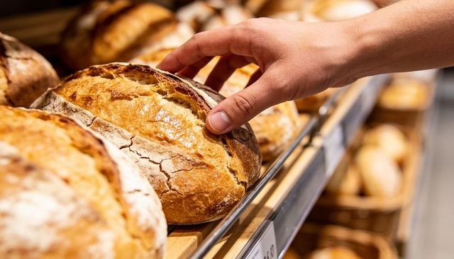 Hand selecting rustic sourdough loaf on bakery shelf with warm crust close-up