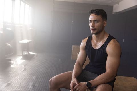 Muscular man resting on plyometric box recovering after intense gym workout for strength