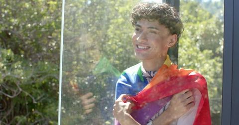 Young Man Embracing Rainbow Pride Flag by Sunny Window