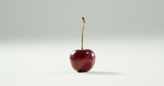 Close up of one fresh red cherry on white floor on white background. Health, diet and food.