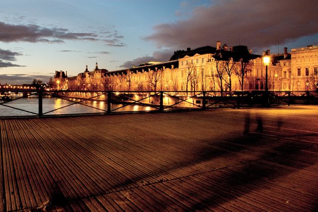 Pont des Arts bridge over the River Seine in Paris illuminated at dusk, capturing the reflections and the historic architecture lining the waterfront. Ideal for use in travel blogs, tourism advertisements, and cultural articles highlighting romantic and picturesque European destinations.