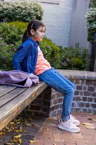 Asian schoolgirl relaxing on bench in courtyard wearing denim jacket and pink sneakers