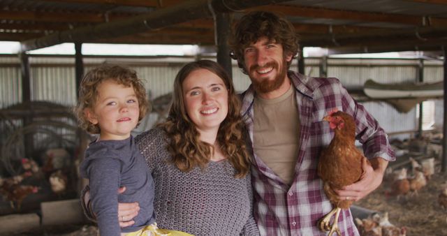 Portrait of smiling caucasian family holding chicken, looking at camera. homesteading, healthy lifestyle on organic farm in the countryside.