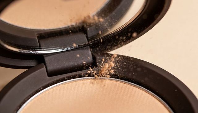 Pressed powder compact releasing fine beige dust with mirror reflection macro beauty