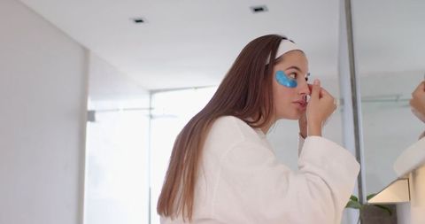 Woman applying under-eye gel patch at bathroom vanity