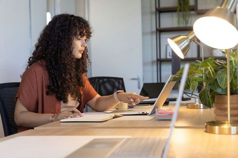 Curly-haired woman pointing at laptop while working at modern wooden desk