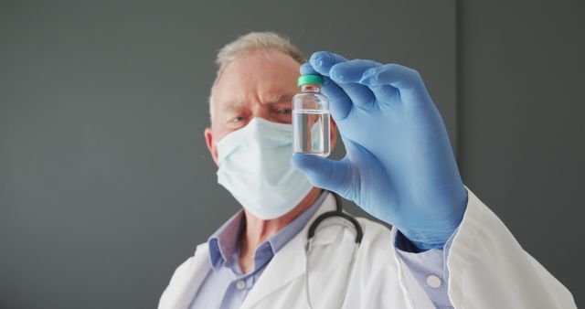 Portrait of caucasian senior male doctor wearing face mask holding covid-19 vaccine. covid-19 vaccine and treatment concept
