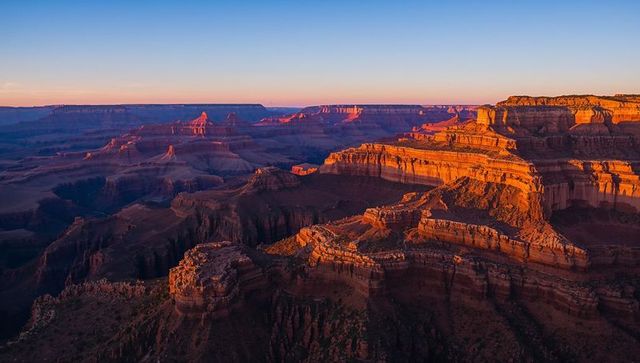 Sunlight bathing layered sandstone cliffs and mesas glowing at sunrise over vast canyon