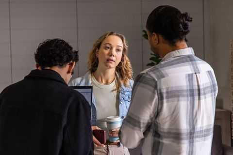 Young woman leading candid team discussion in modern office lounge holding travel cup