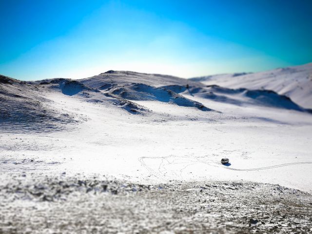 Solitary vehicle parked on snowy desert terrain with bright sky above. Sparse tracks visible in the snow emphasizing the remote and isolated nature of the location. Ideal for use in articles or advertisements about winter travel, adventure, solitude, or off-road journeys.