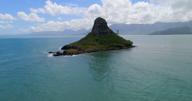 An isolated island with lush greenery sitting in the midst of a vast turquoise ocean. Snow-capped mountains are visible in the distance, adding to the island's scenic beauty. Perfect for travel guides, adventure blogs, nature documentaries, and eco-tourism promotions.