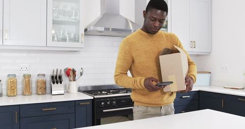 Man scanning package in modern kitchen with smartphone