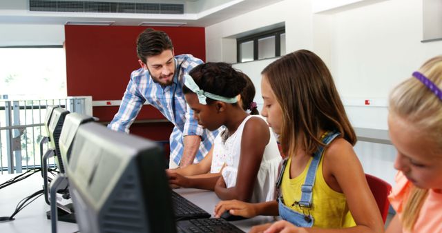 Image of a teacher assisting a group of diverse students in a computer lab. Helpful for illustrating modern education trends, technology in classrooms, teamwork in learning environments, or teacher-student interaction. Suitable for educational articles, blogs, or advertisements promoting technology in education.