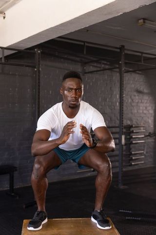 Athletic man executing squat jump on plyometric box at gym