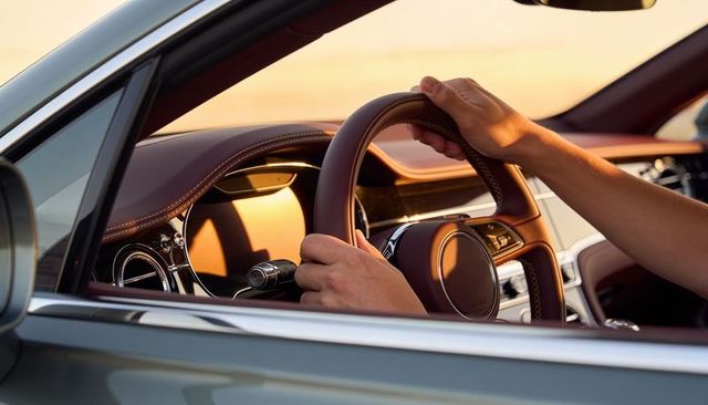 Hands gripping leather steering wheel of luxury car at sunset, close-up interior detail