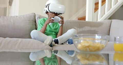 African American child wearing VR headset playing video game on living room sofa at home