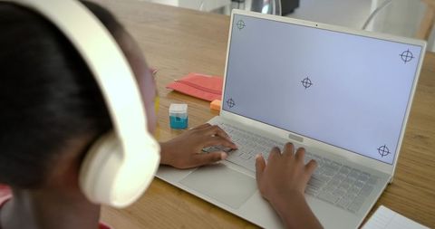 African american teen wearing headphones typing on laptop at home study desk