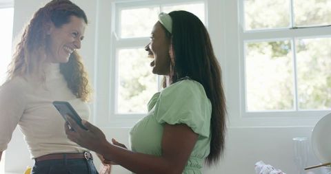 Diverse Female Friends Enjoying Laughter and Smartphone in Sunny Kitchen