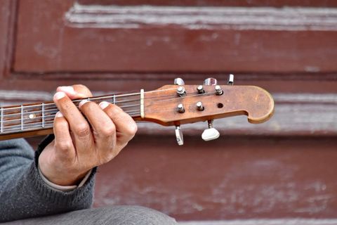 Close-Up of Person's Hand Playing Guitar Against Rustic Background