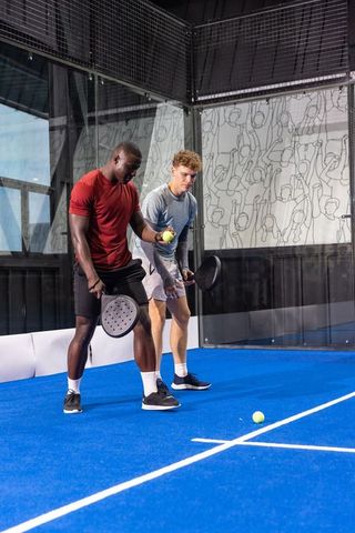 Mixed-race partners practicing paddle doubles on blue indoor court for fitness, teamwork
