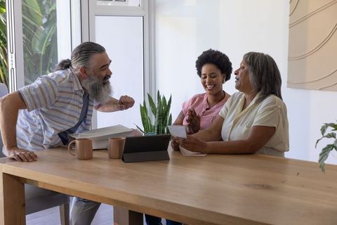 Multigenerational family laughing and reading letter at sunny dining table with tablet