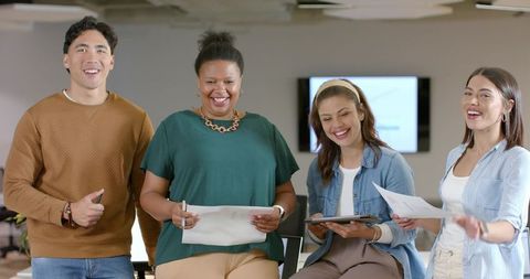 Diverse team collaborating in modern office holding tablet and documents, smiling