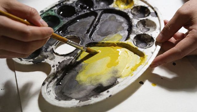 Mixing vivid yellow paint on worn plastic palette, close-up of brush and artist hands