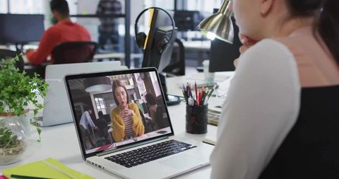 Open-plan office worker joining remote video call on laptop for coworking collaboration