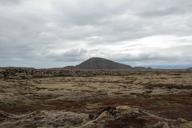 Depicts a remote, barren volcanic landscape under an overcast sky, providing a feel of solitude and desolation. This image can be used for travel content, nature blogs, environmental documentaries, or evocative artwork requiring rugged, otherworldly scenery.