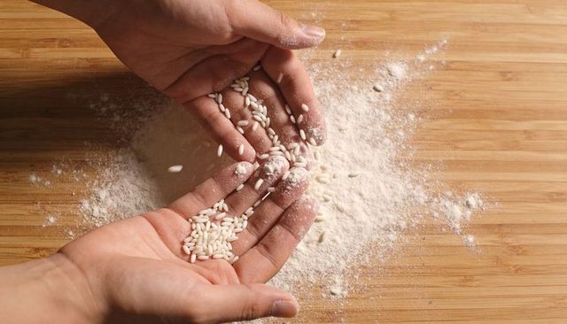 Catching and releasing short-grain rice over flour-dusted bamboo cutting board close-up