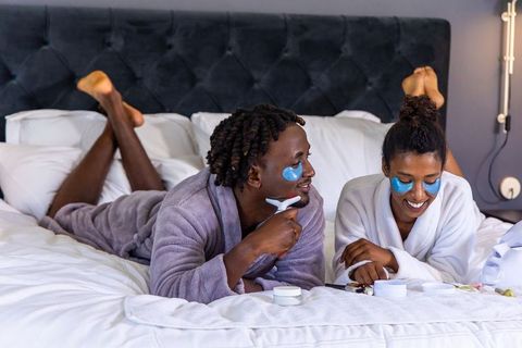 African couple enjoying at-home spa ritual with under-eye patches and facial massager
