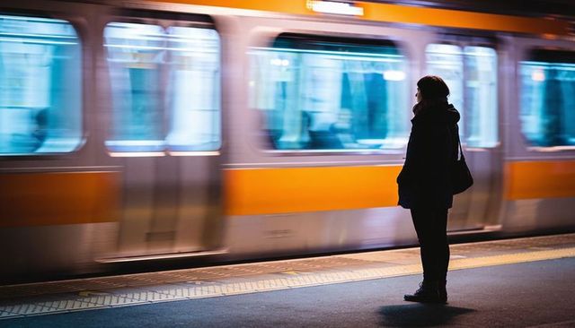 Solitary commuter watching passing orange train at night, subway platform motion blur
