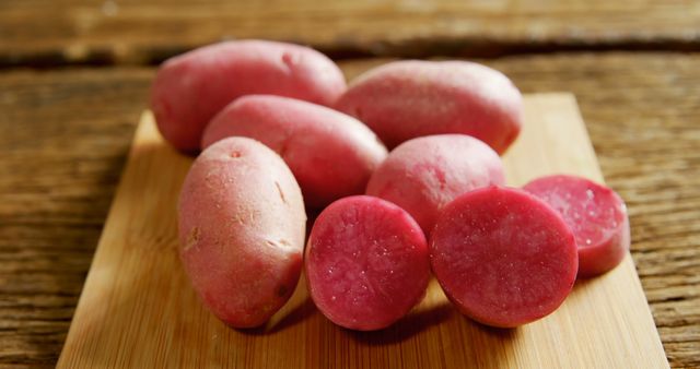 Red potatoes are neatly arranged on a wooden cutting board, showcasing their vibrant pinkish flesh. Their smooth texture and rich color indicate freshness, ideal for culinary uses.