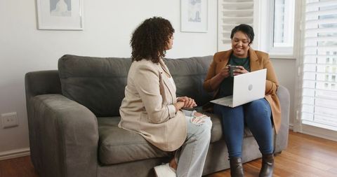 African American Women Collaborating on Laptop Over Coffee in Contemporary Home Lounge