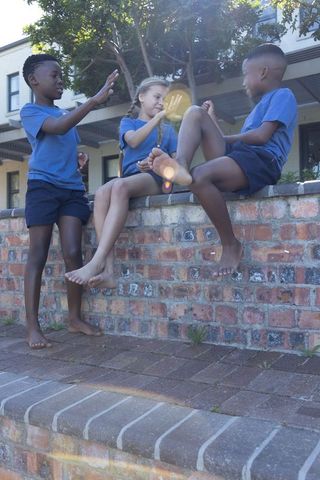 Diverse children chatting and playing on brick wall with sunlit lens flare and barefoot fun
