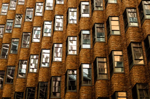 Close-up of brick building facade with staggered windows reflecting sunset light. Ideal for concepts of urban design, architecture details, contemporary buildings, and cityscape aesthetics. Also suitable for background, pattern, or texture projects.