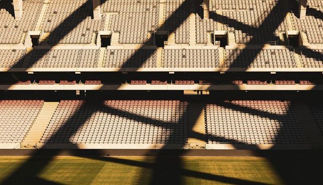 Empty stadium seating casting dramatic angular shadows over sunlit red tiered seats