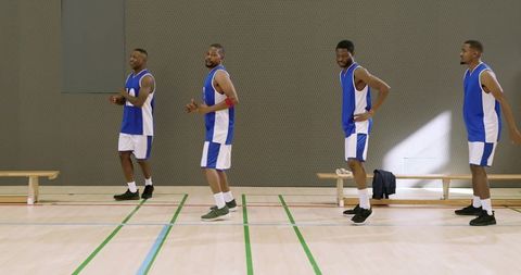 Standing basketball team lineup practicing on indoor court wearing blue jerseys, sneakers