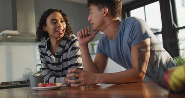 Two friends chatting and enjoying each other's company in a modern kitchen. They are dressed in casual clothing and one of them is holding a mug. This image is great for websites and blogs focusing on friendship, social interactions, modern living spaces, and casual lifestyles.