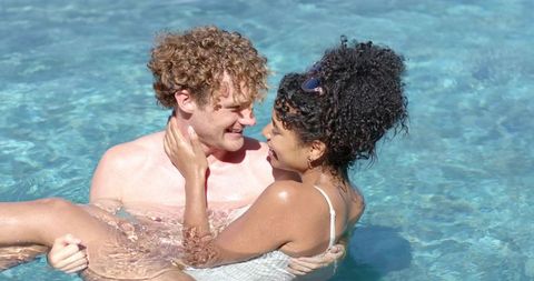 Young couple embracing and laughing in sunlit resort pool during romantic summer getaway