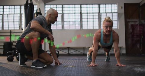 Trainer coaching client performing plank in sunlit gym with chart overlay and kettlebells