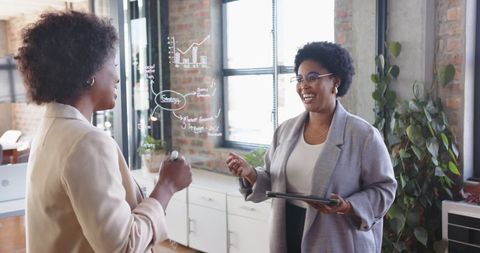 Businesswomen analyzing charts on transparent board in modern office