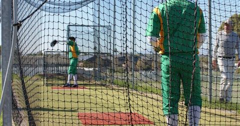 Baseball players practicing in outdoor batting cage with coach observing and training