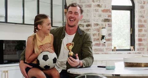Father and Daughter Bonding over Soccer in Kitchen Setting