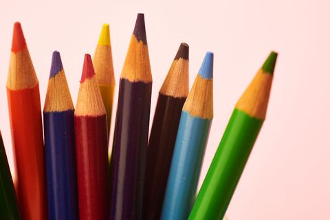 Colorful sharpened colored pencils standing against soft pink background