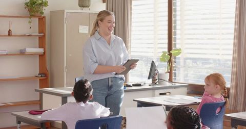 Female teacher using digital tablet teaching engaged students in classroom