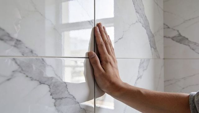 Male hand pressing glossy marble tile showing grout detail, reflective surface and window light
