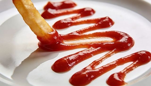 Dipping thick-cut french fry into zigzag ketchup, glossy close-up of condiment swirl