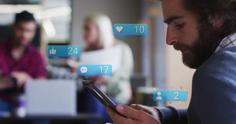 Bearded man scrolling smartphone with social notifications floating in coworking office