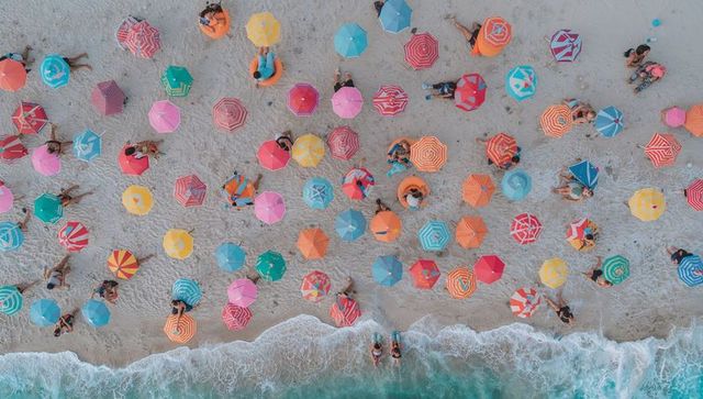 Colorful aerial view of crowded beach with patterned parasols and turquoise waves
